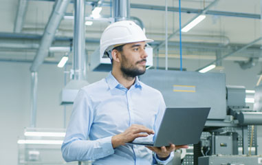 chico con casco y ordenador en una fábrica