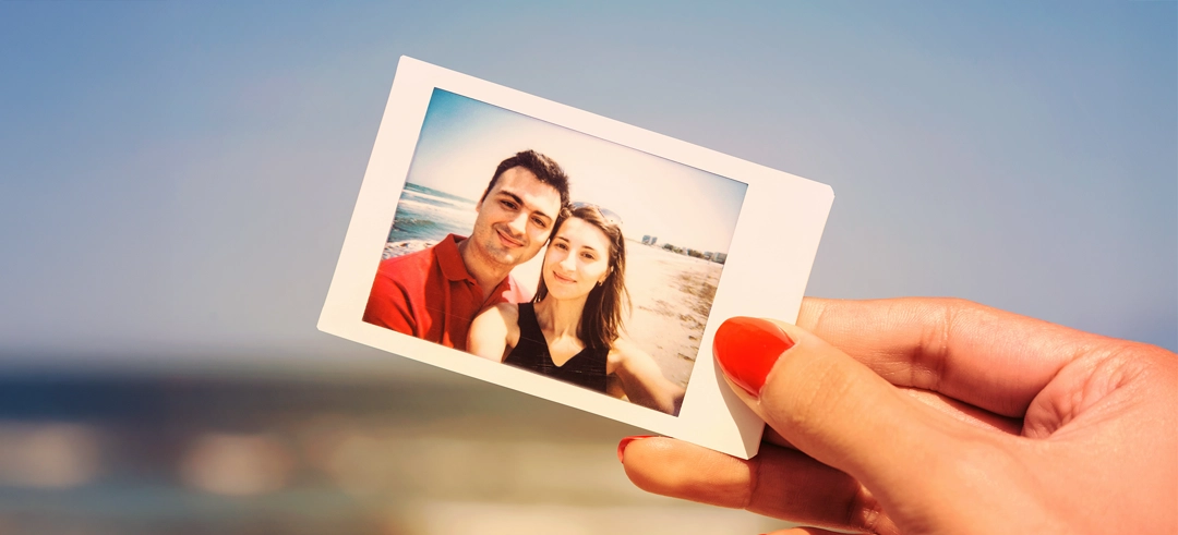 Mano sosteniendo una foto de una pareja en la playa con el mar de fondo